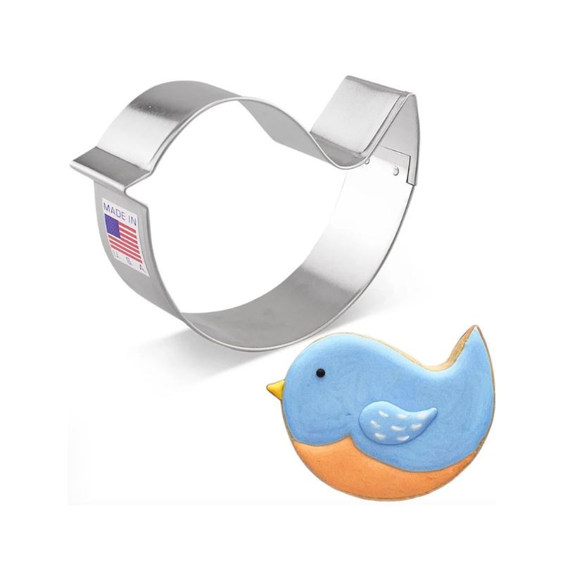 Metal bird cookie cutter with american flag sticker next to a blue deocrated with royal icing cookie and orange belly and yellow beak