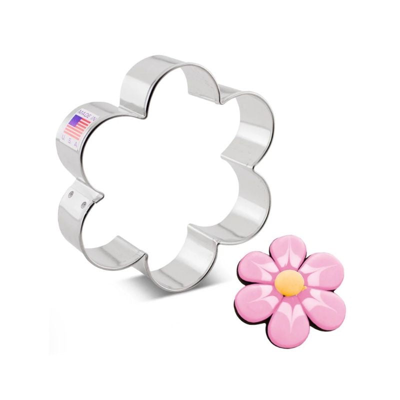 metal flower cookie cutter with flag sticker net to sugar cookie with different shades of pink royal icing and yellow circle