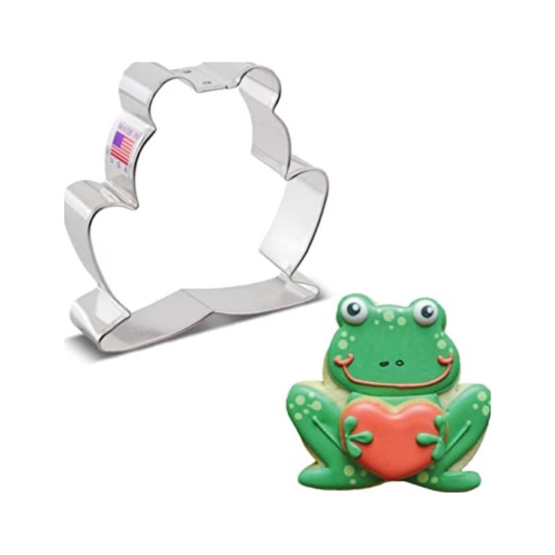 Metal cookie cutter in the shape of a frog next to a sugar cookie decorated with royal icing in green and holding a red heart