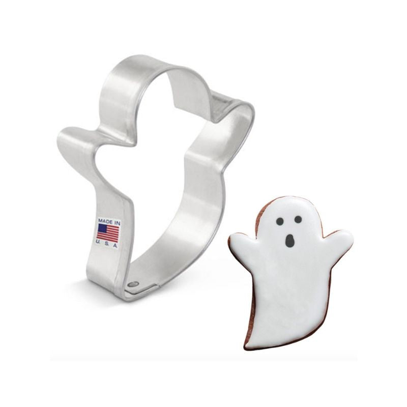 Stainless steel cookie cutter in the shape of a mini ghost and small ghost cookie beside with white royal icing and black details