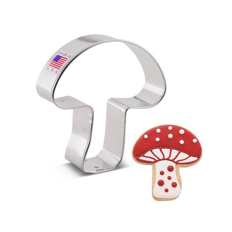 Metal mushroom cookie cutter with made in usa sticker with flag next to a sugar cookie mushroom with red icing and white polkadots 