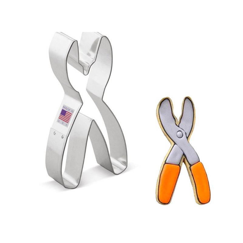 Metal cookie cutter in the shape of pliers with American flag sticker on side next to sugar cooie iced with silver tops and orange grip handles