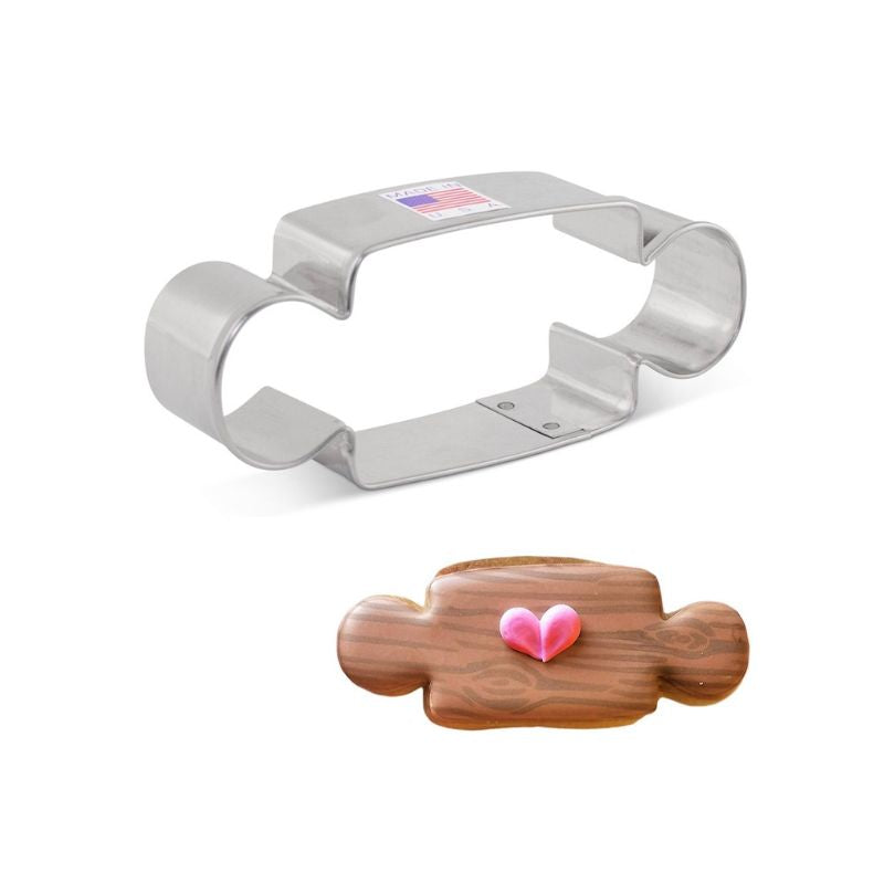 Metal rolling pin cookie cutter with flag sticker on top next to wood grain royal icing sugar cookie and pink heart