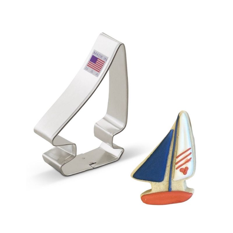 Made in the USA sticker with American flag metal cookie cutter in the shape of a sailboat next to a cookie with royal icing decorations in blue which and red