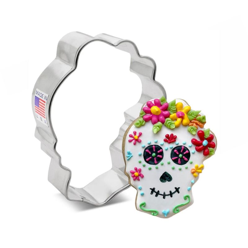 Metal cookie cutter in the shape of a sugar skull with a decorated sugar cookie with flowers and bright colour details