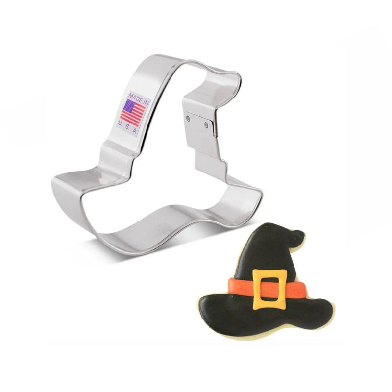 Stainless steel witch hat with made in USA and American flag sticker on side beside a sugar cookie with black royal icing icing and yellow and orange details