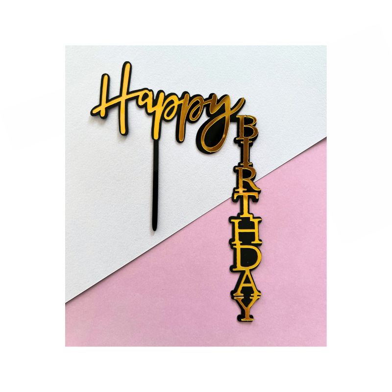 A birthday cake topper named "Happy Birthday Black side" features the word "Happy" written in cursive in black with a gold outline, and the word "Birthday" vertically in block letters, also in black with a gold outline. The topper is set against a split background of white and pink.