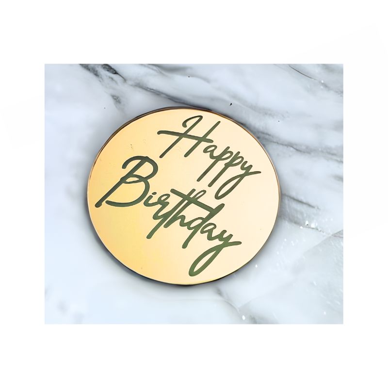 gold circle cake charm with happy birthday written on and dic in on marble background