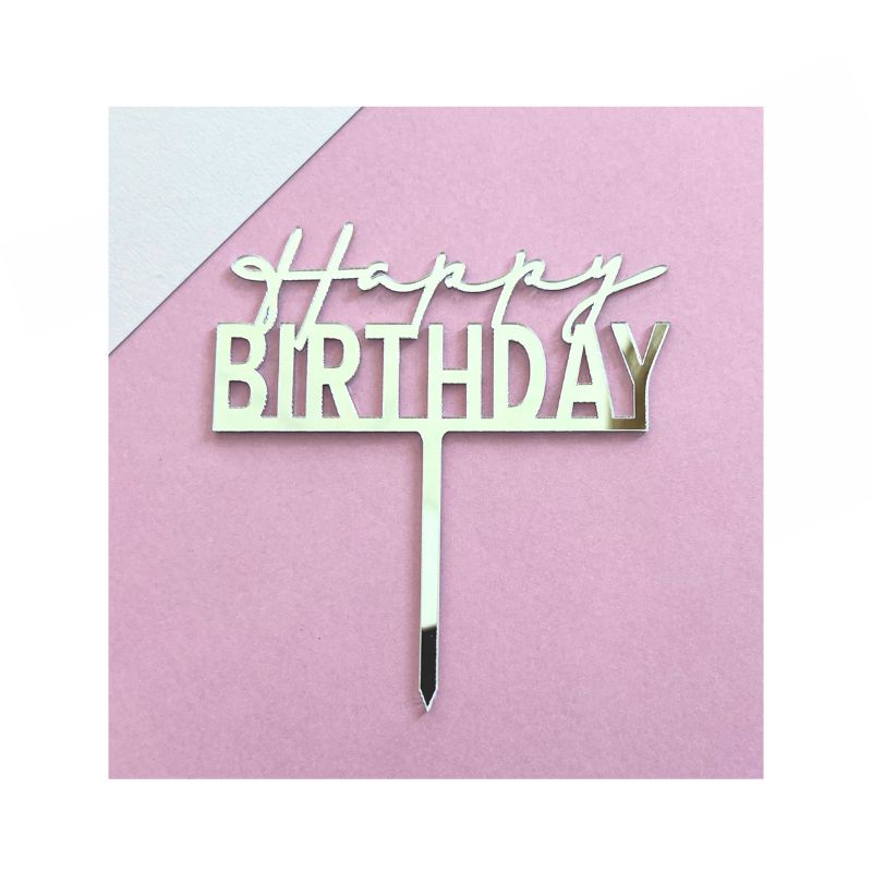 The "Silver Happy Birthday" cake topper features the words "Happy Birthday" written in an elegant, cursive font. Made of a metallic material, this topper is beautifully placed on a light pink surface. 