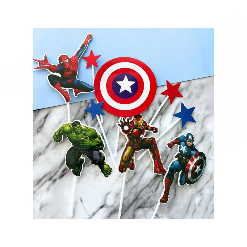 The Super Hero Cake Topper set, featuring five designs including Spider-Man, Captain America's shield, stars, the Hulk, Iron Man, and Captain America himself, is displayed against a blue and marble backdrop.