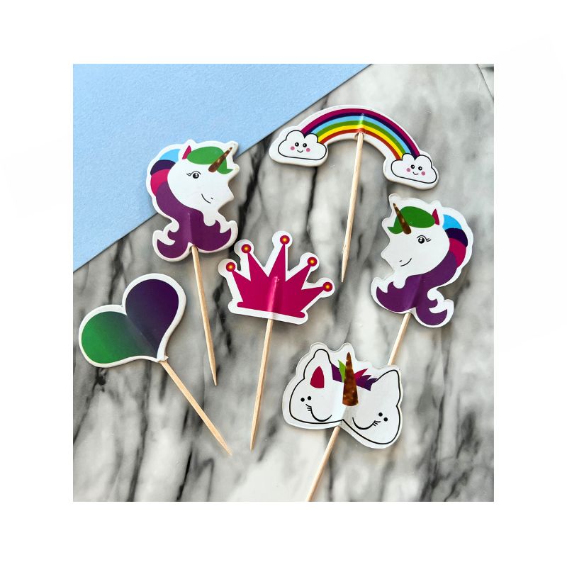 3 unicorn cupcake toppers with one rainbow and one heart and crown with tooth pick for cupcake toppers on marble background