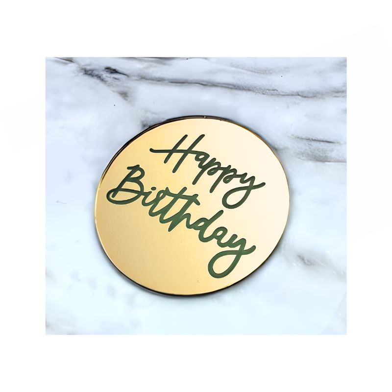 Gold Circle cake charm with happy birthday written in hand writing on marble background