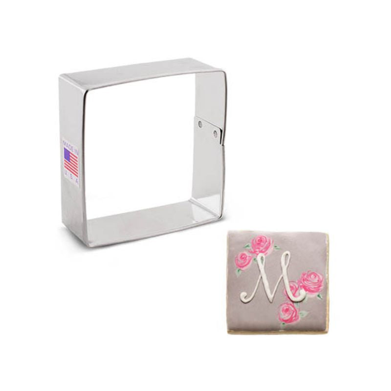 Metal cookie cutter in the shape of a small square beside a decorated cookie in taupe colour with roses in pink