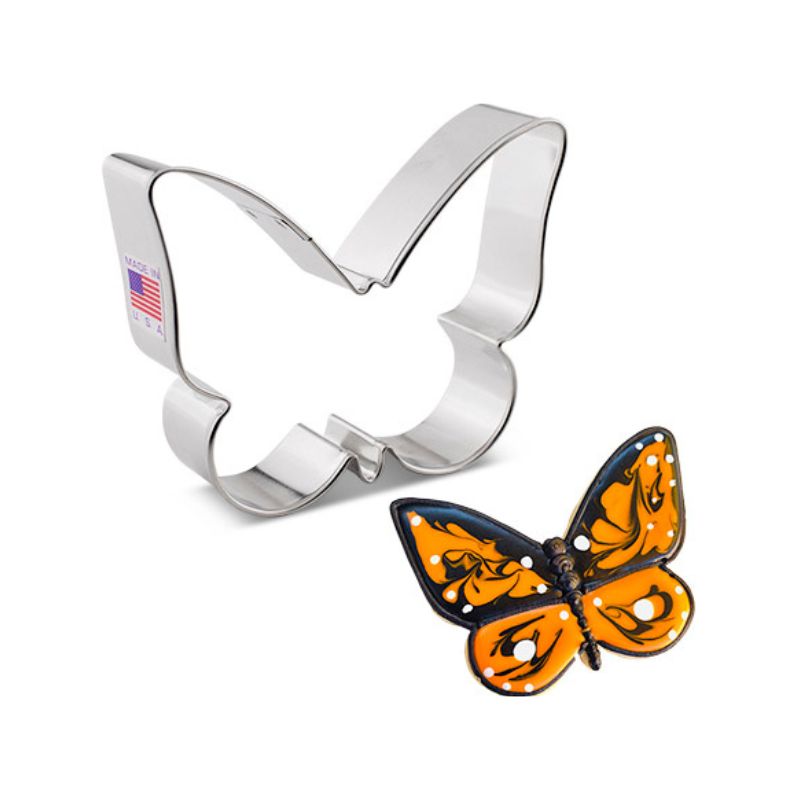 Stainless steel cookie cutter in the shape of a cute butterfly next to a sugar cookie with orange and black icing