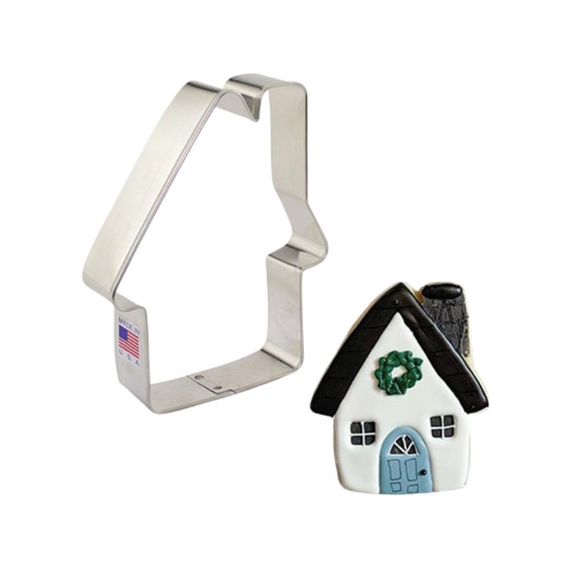 stainless steel cookie cutter in the shape of a house and cookie that has been decorated with royal icing in white blue and black with green wreath