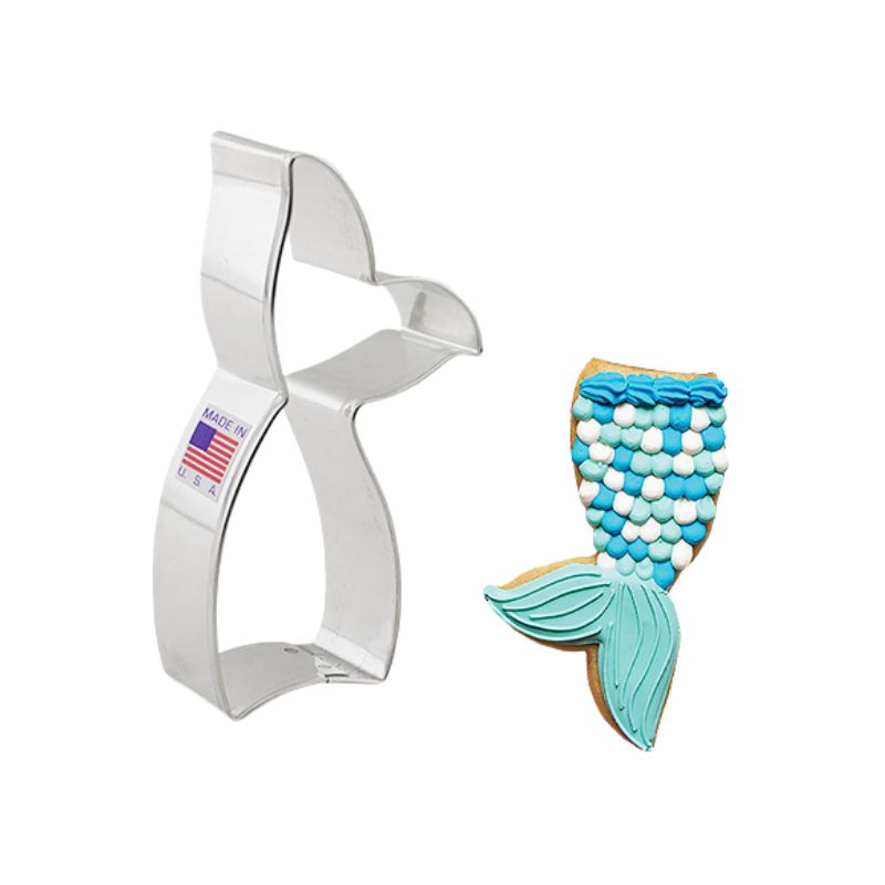 Metal cookie cutter made in the USA with flag sticker and beside mermaid tail cookie decorated with royal icing in teals blues and whites