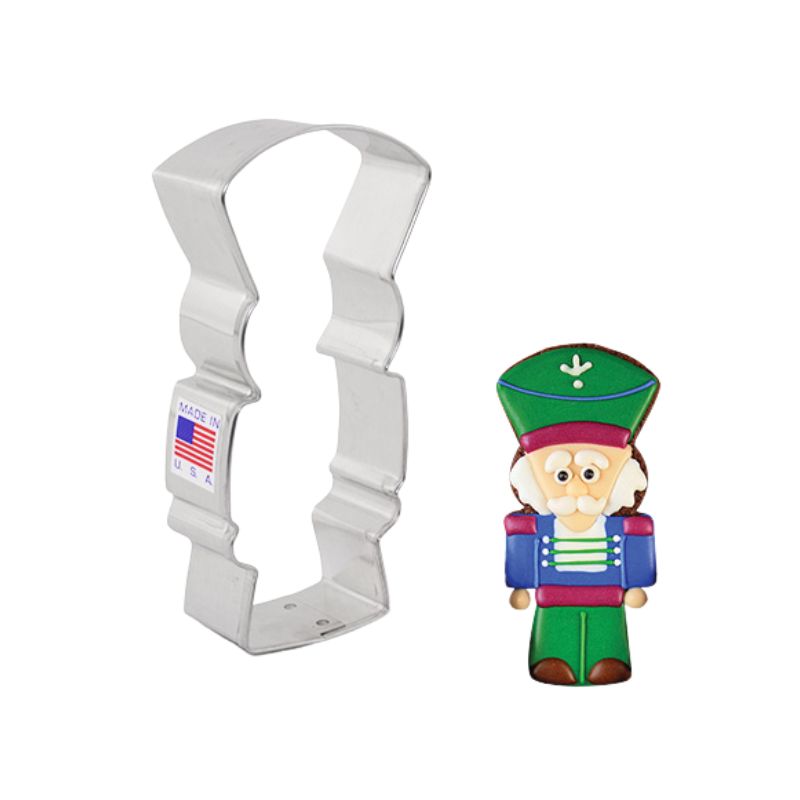 Made in the USA with American flag sticker on metal cookie cutter with decorated nutcracker cookie beside with green and burgundy hat and blue and white shirt and green pants