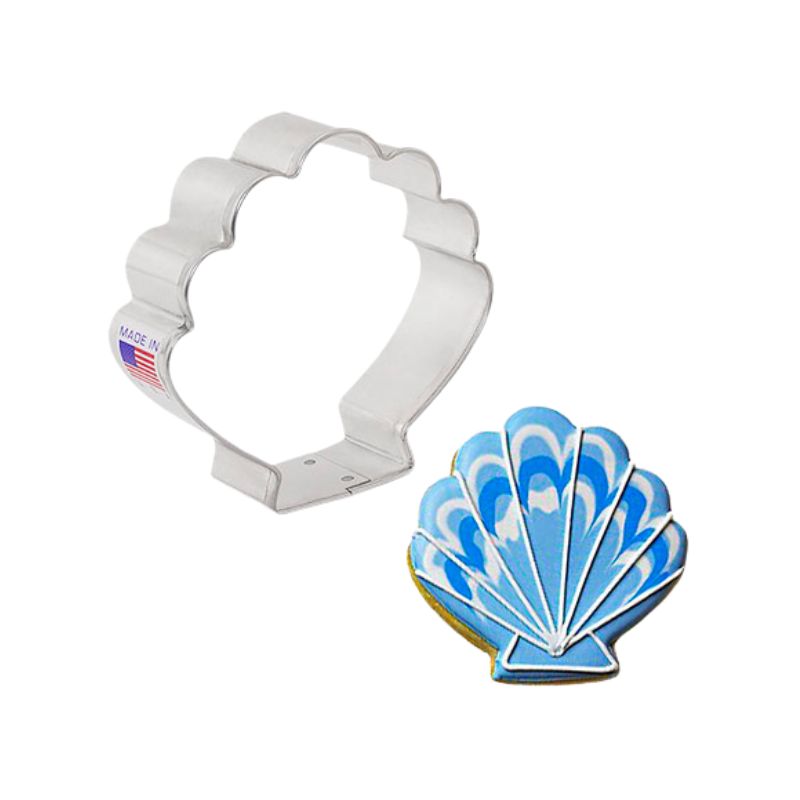 Metal cookie cutter in the shape of a seashell and beside a blue seashell with white and navy swirls and white outside details