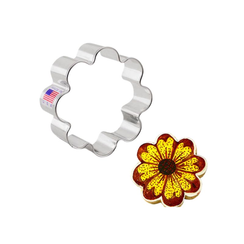 Metal cookie cutter in the shape of a flower next to a cookie that is iced with royal icing in red and yellow