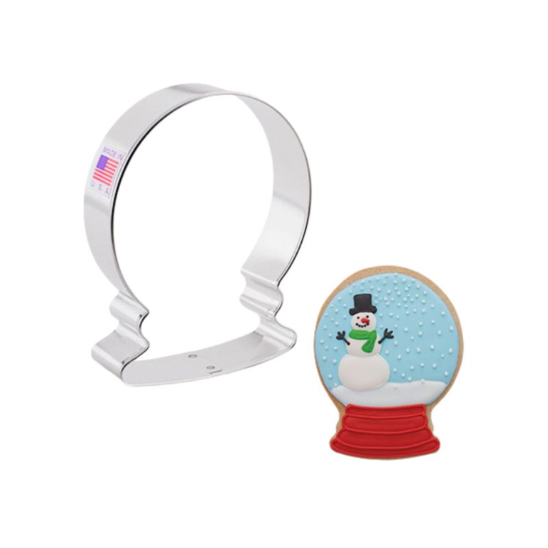 stainless steel cookie cutter shaped like a Christmas snow globe and next to a decorated globe with blue background and red base with a snowman and snow falling royal icing