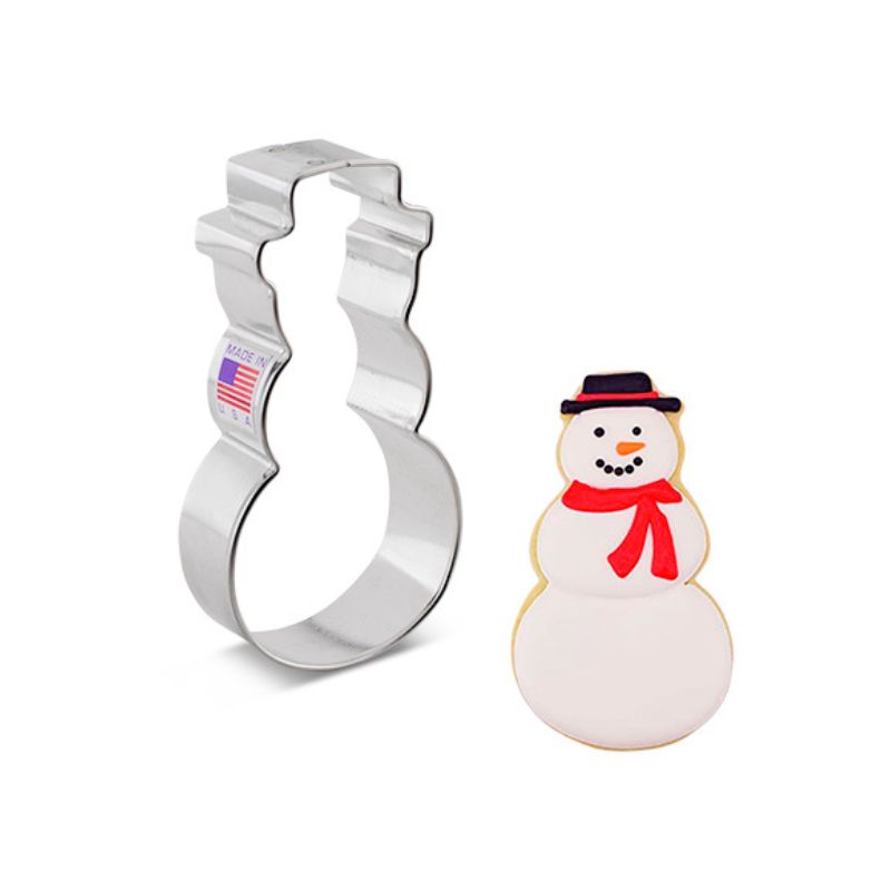 metal snowman cookie cutter next to a sugar cookie that is decorated with white royal icing red scarf and black top hat