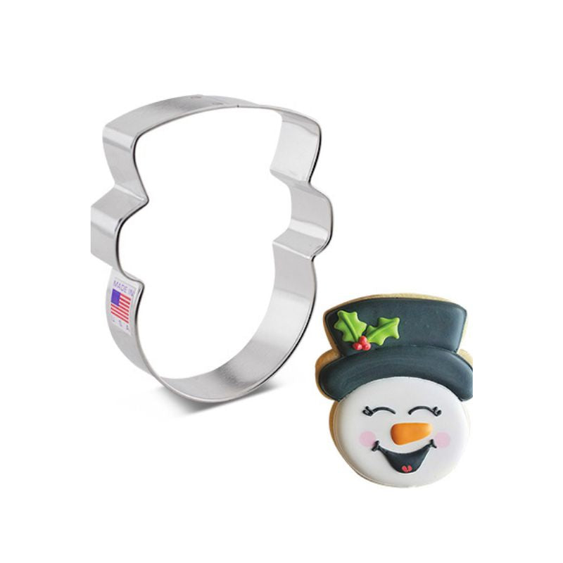 snowman metal cookie cutter shaped like snowman head and is next to a decorated sugar cookie snowman head with black top hat white face and orange nose