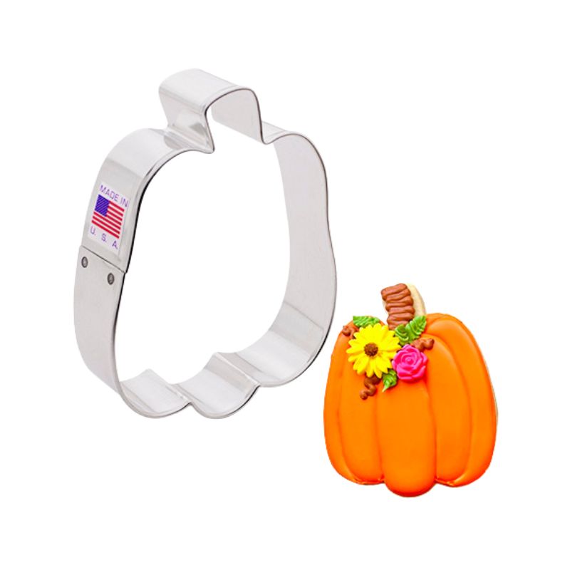 Stainless steel cookie cutter in the shape of a tall pumpkin next to a decorated pumpkin with orange icing and flowers on side