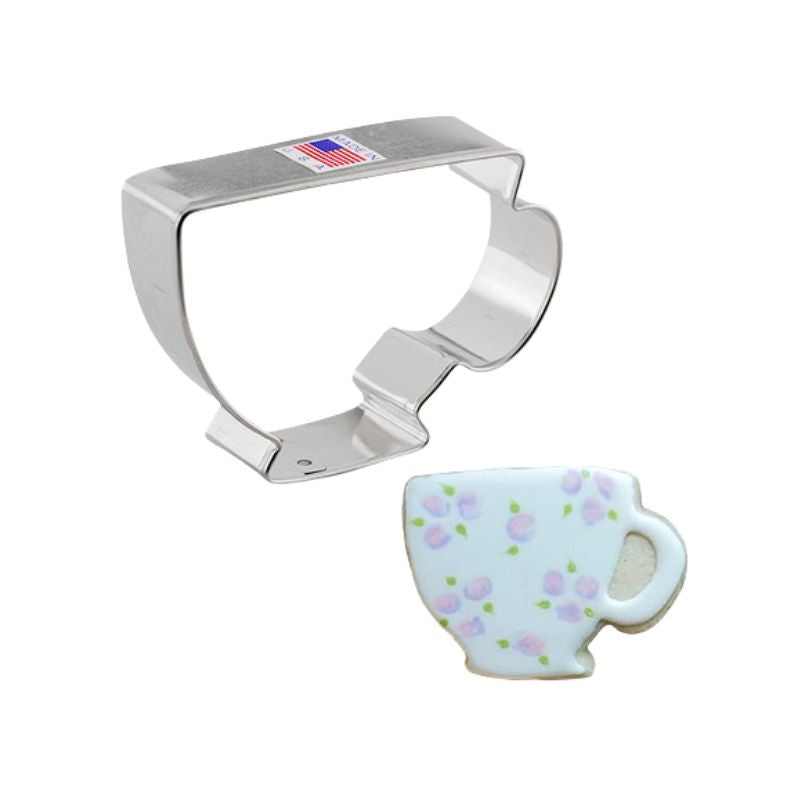 Stainless steel cookie cutter in the shape of a teacup and beside a cup with roses and leaves on it