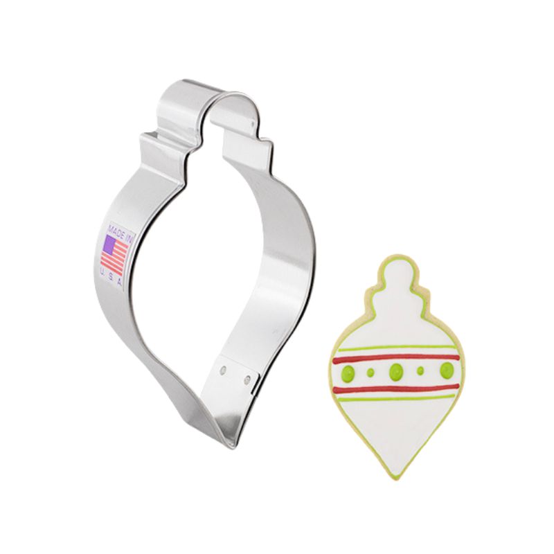 Metal cookie cutter in the shape of a Christmas ornament and beside a decorated cookie with royal icing in white red and green