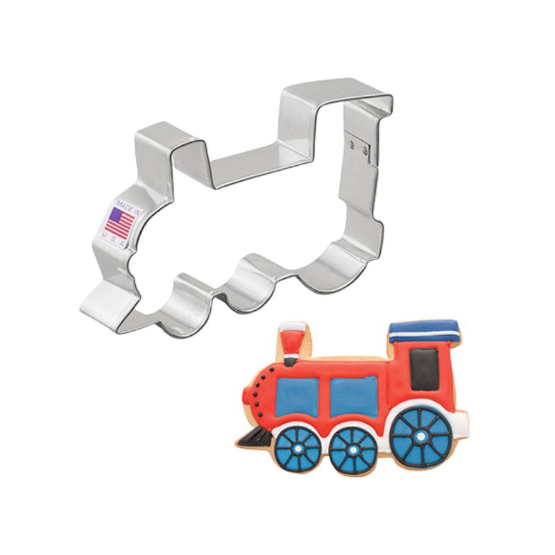 Metal train cookie cutter with American flag on beside a red royal icing train cookie with blue wheels