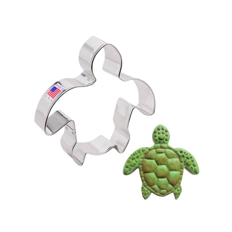 Made in the USA metal cookie cutter nest to a green decorated turtle with lighter green details in royal icing made with meringue powder