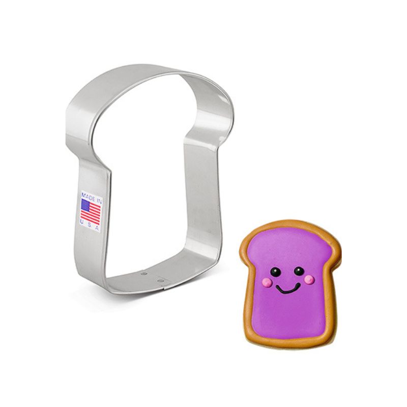 Metal slice of bread cookie cutter made in the usa sticker beside a bread with brown edges and purple jam on top with black smile